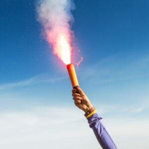 A woman in the wild mountains gives a distress signal SOS using Falsch feuer torch from which comes a bright flame and orange smoke, Concept of emergency situation during hike in the woods